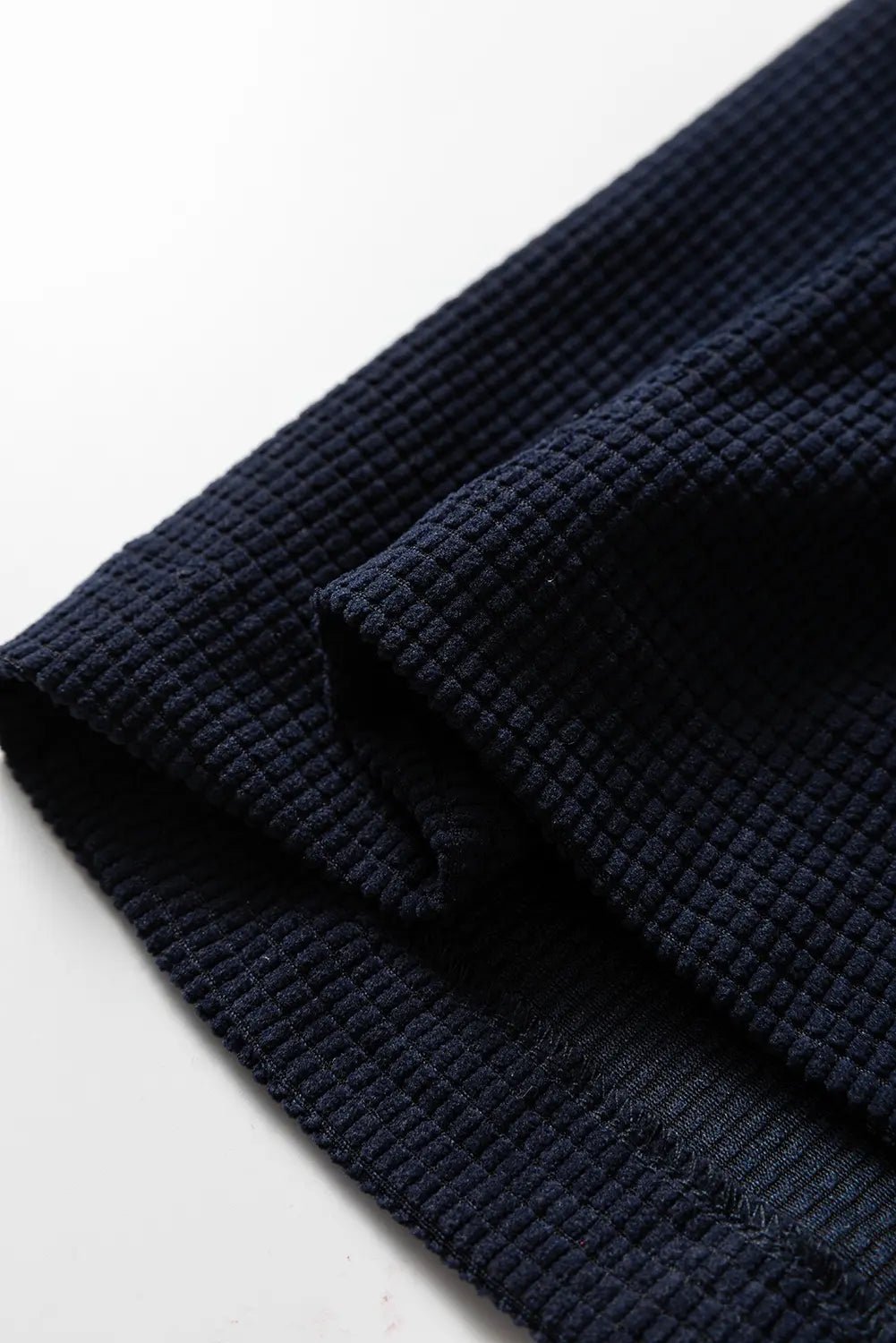 A close-up of dark navy blue waffle-knit fabric, showing its textured grid pattern and folded edges against a plain white background.