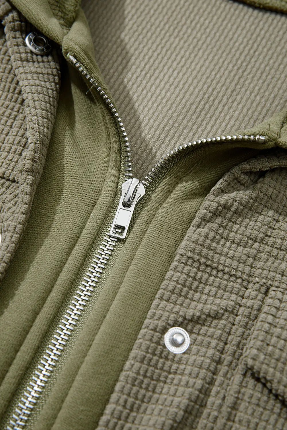 Close-up of a green textured jacket with a zipper and button.