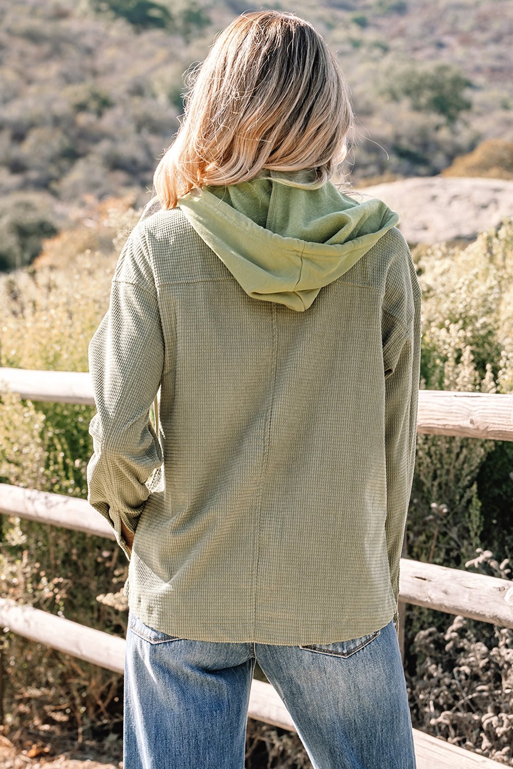 Person wearing a green jacket with a hood standing in a natural setting.