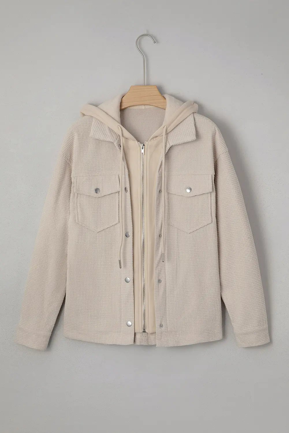 Beige jacket with a hood on a wooden hanger against a gray background.
