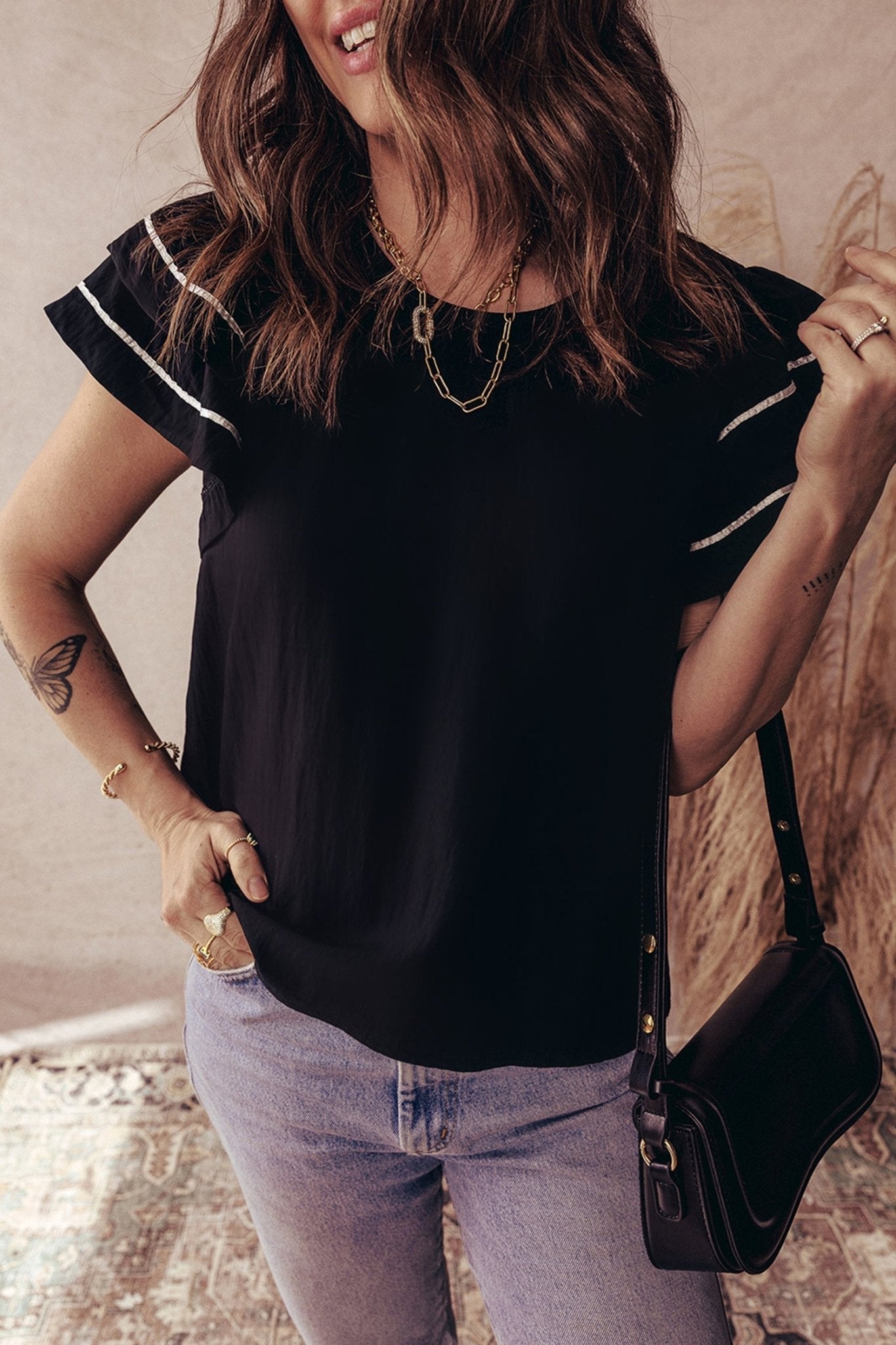 Woman wearing a black top with white trim and light blue jeans, holding a black handbag.