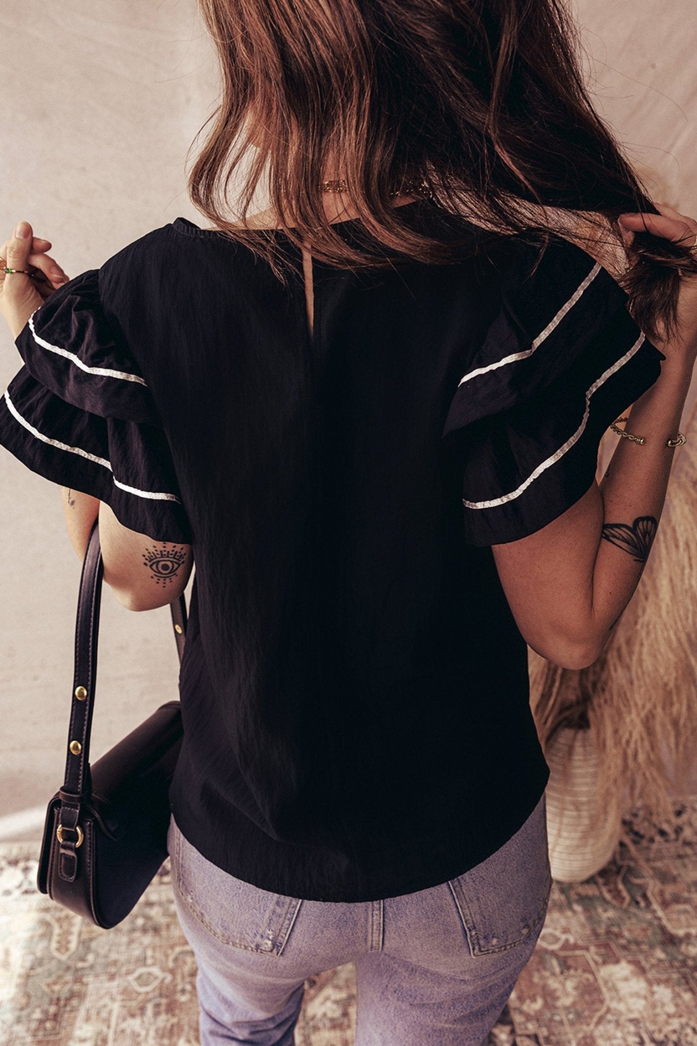 Person wearing a black blouse with white trim, holding a black handbag.