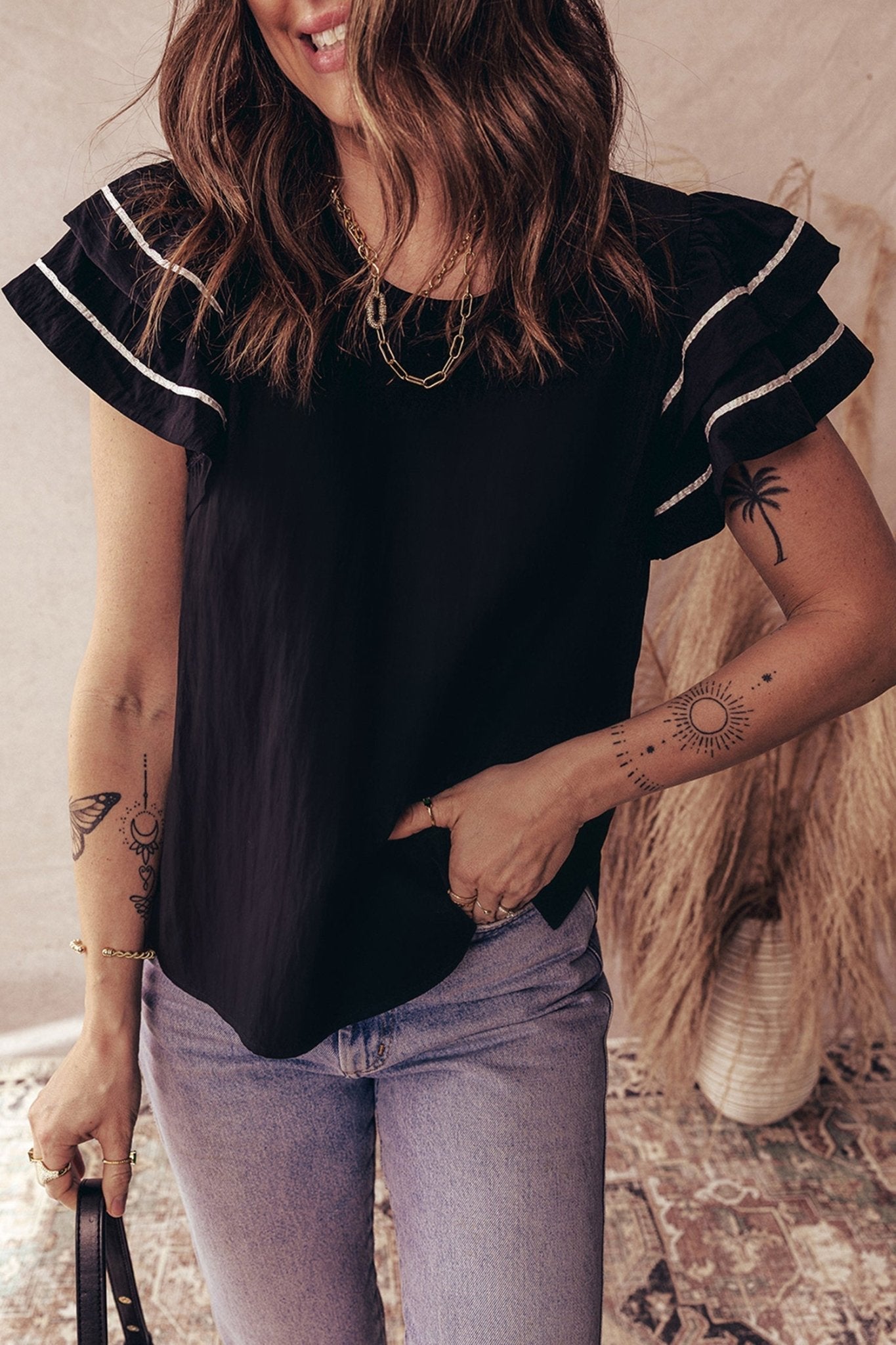 Person wearing a black top with ruffled sleeves and light blue jeans indoors.