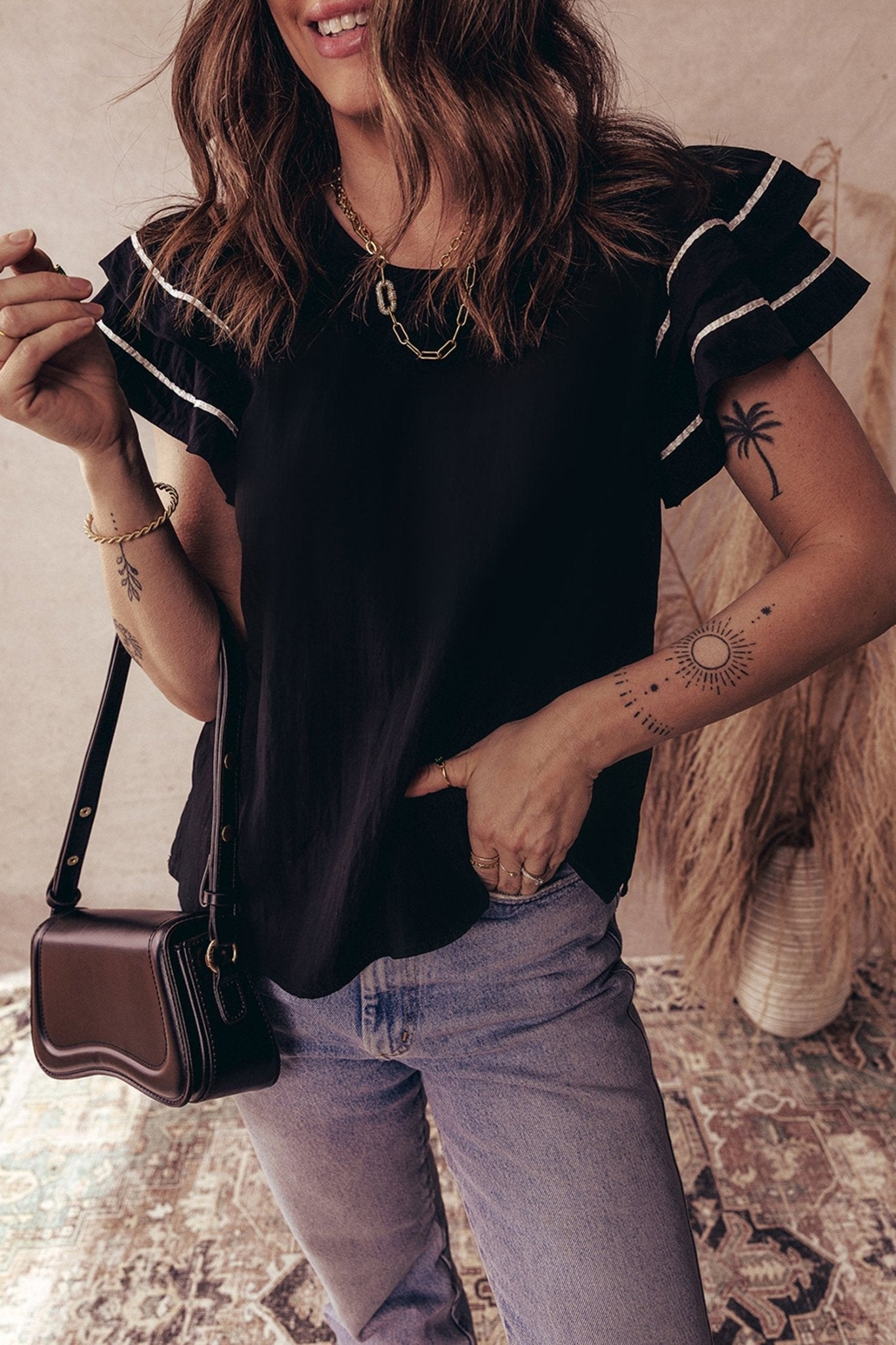 Woman wearing a black top with ruffled sleeves and light blue jeans, holding a brown handbag.