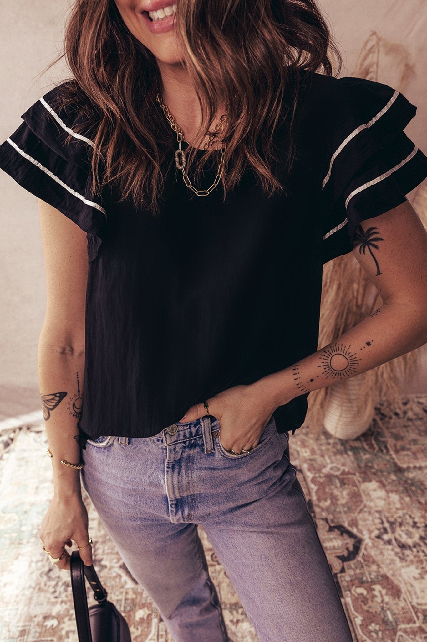 Woman wearing a black top with white trim and blue jeans, standing on a patterned rug.