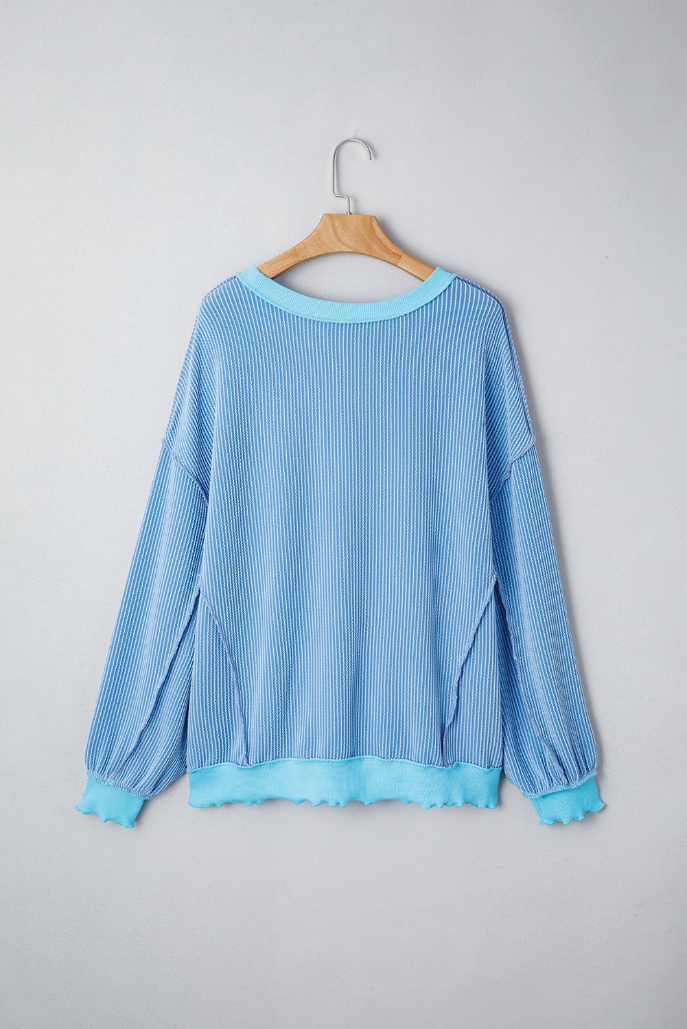 Blue ribbed sweater on a wooden hanger against a gray background