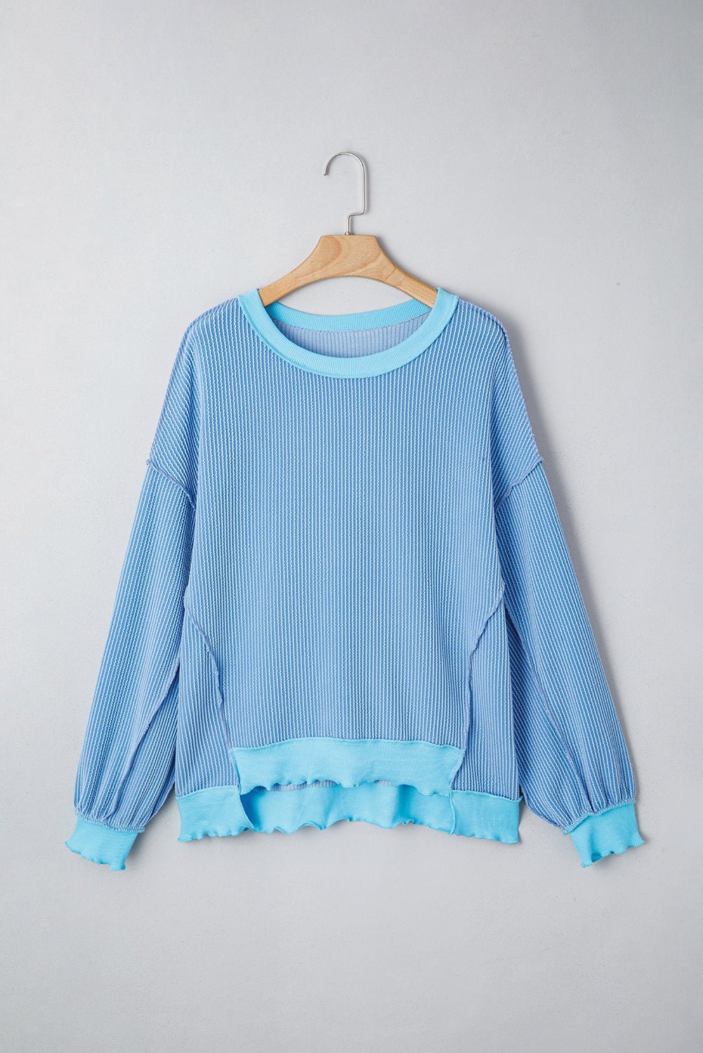 Blue ribbed sweater on a wooden hanger against a gray background