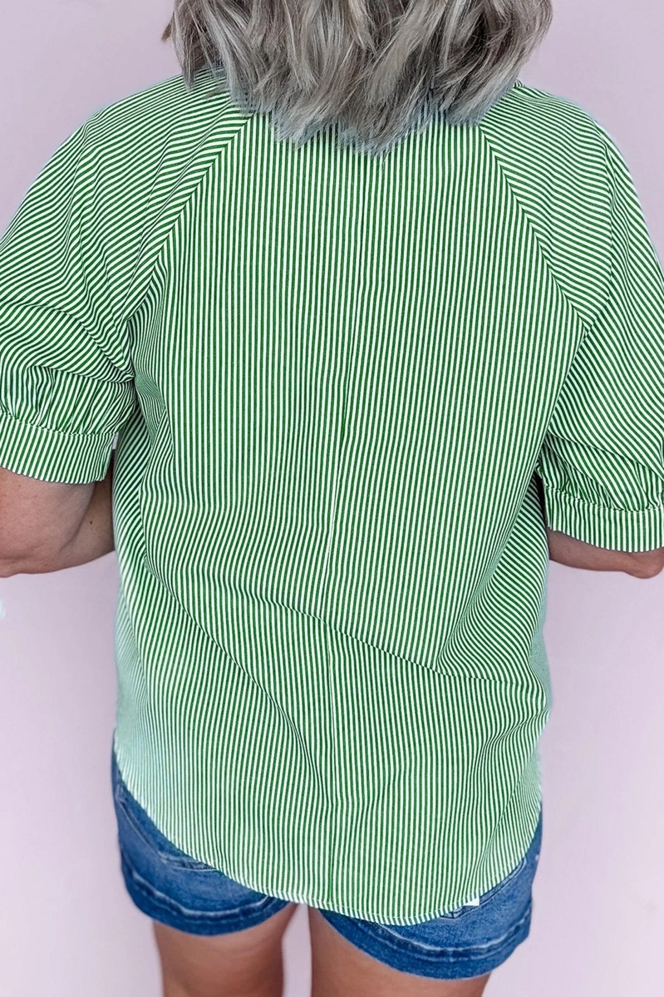Person wearing a green and white striped shirt with blue shorts on a white background