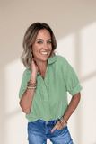 Woman wearing a green striped shirt and blue jeans against a beige background