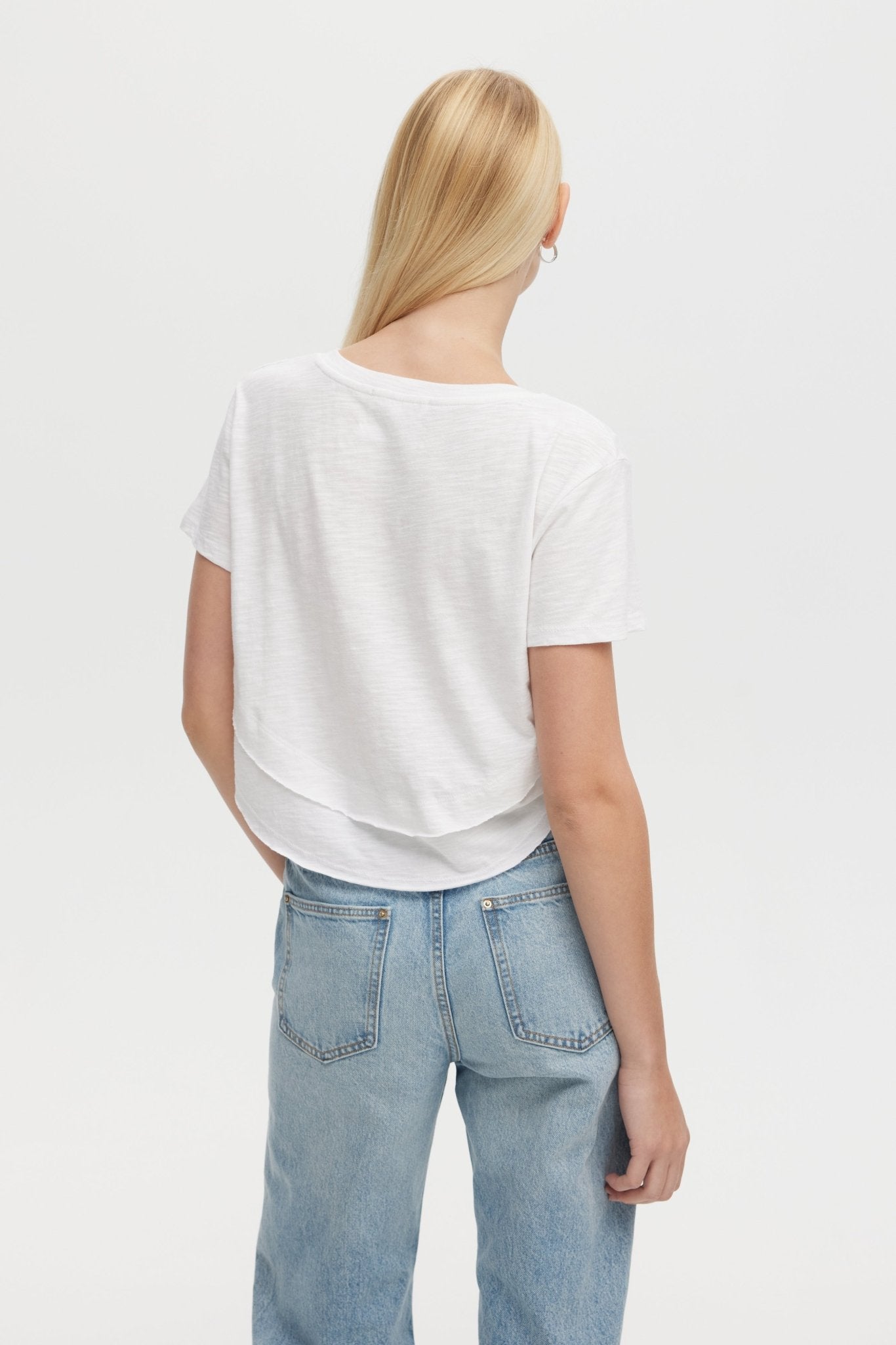 Person wearing a white t-shirt and light blue jeans on a plain background