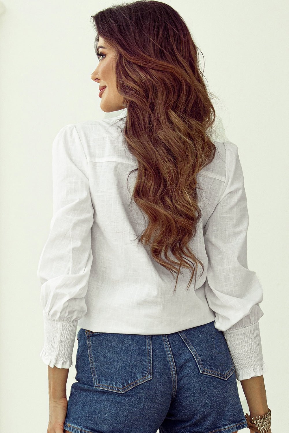 Woman wearing a white blouse and blue jeans with wavy hair on a plain background