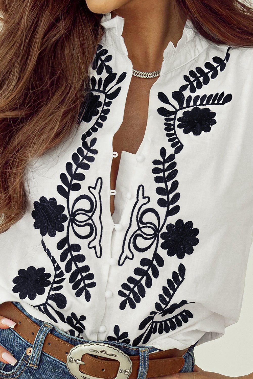 White blouse with black floral embroidery worn by a person.
