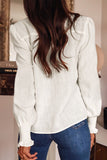 Person wearing a white blouse with long sleeves and blue jeans in an indoor setting.