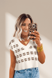 Woman taking a mirror selfie wearing a white sweater with brown patterns, blue jeans, and holding a leopard print phone case.