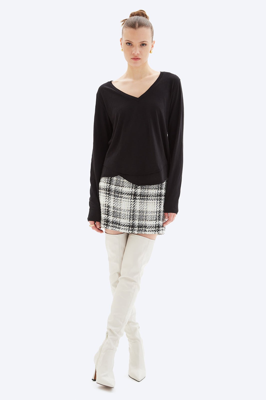Woman wearing a black long-sleeve top, plaid skirt, and white knee-high boots on a white background
