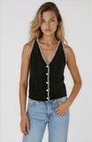 Woman wearing a black sleeveless top with white buttons and light blue jeans on a white background