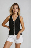Woman wearing a black sleeveless top with white buttons and white shorts on a plain background