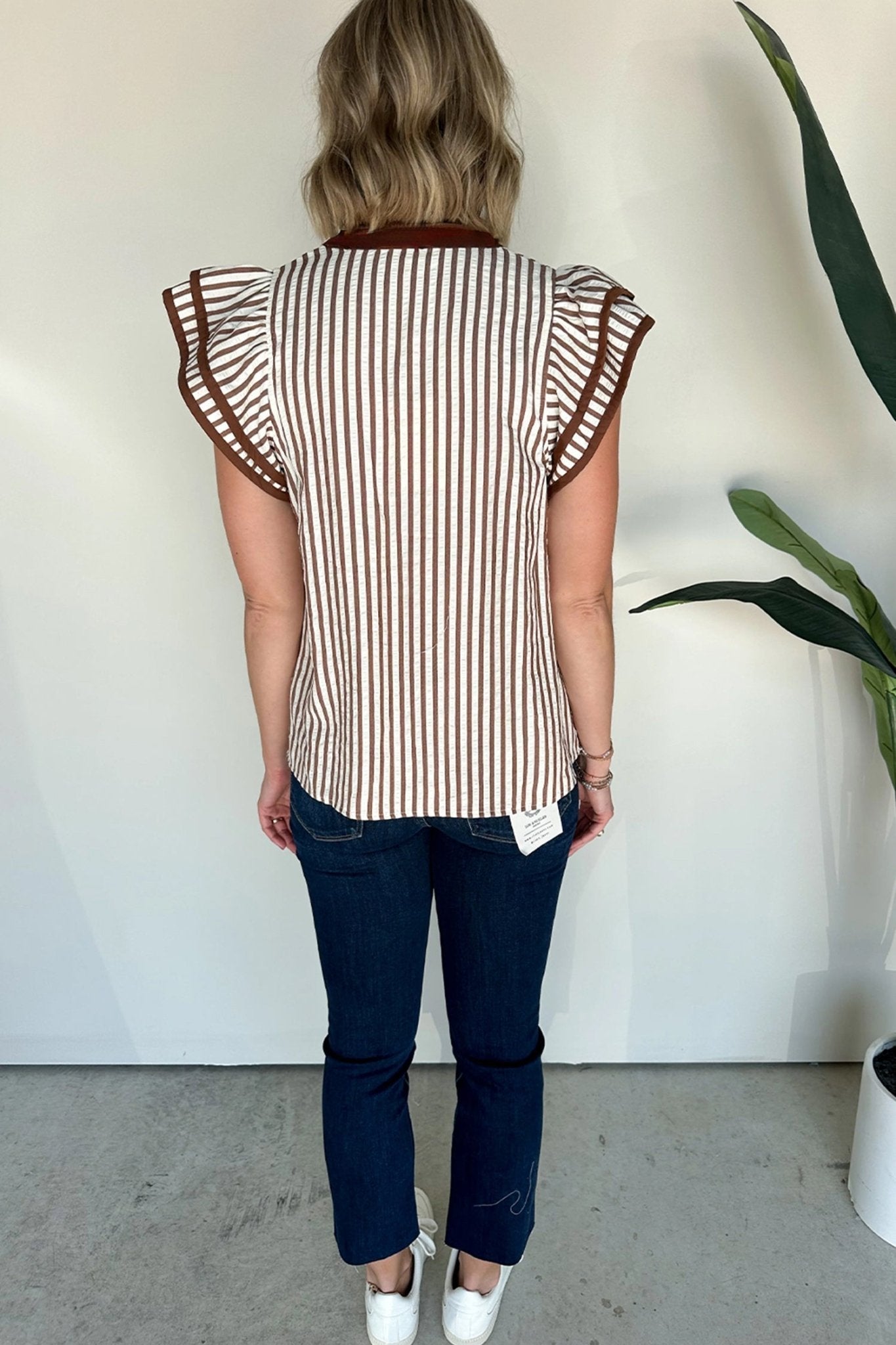Woman wearing a striped shirt with ruffled sleeves against a white wall.