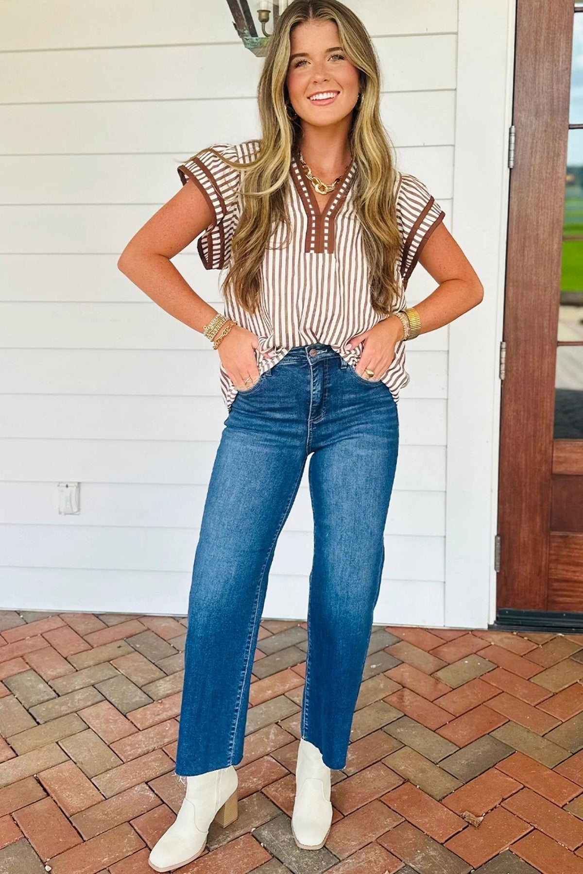 Woman wearing a striped shirt and blue jeans standing on a brick patio.