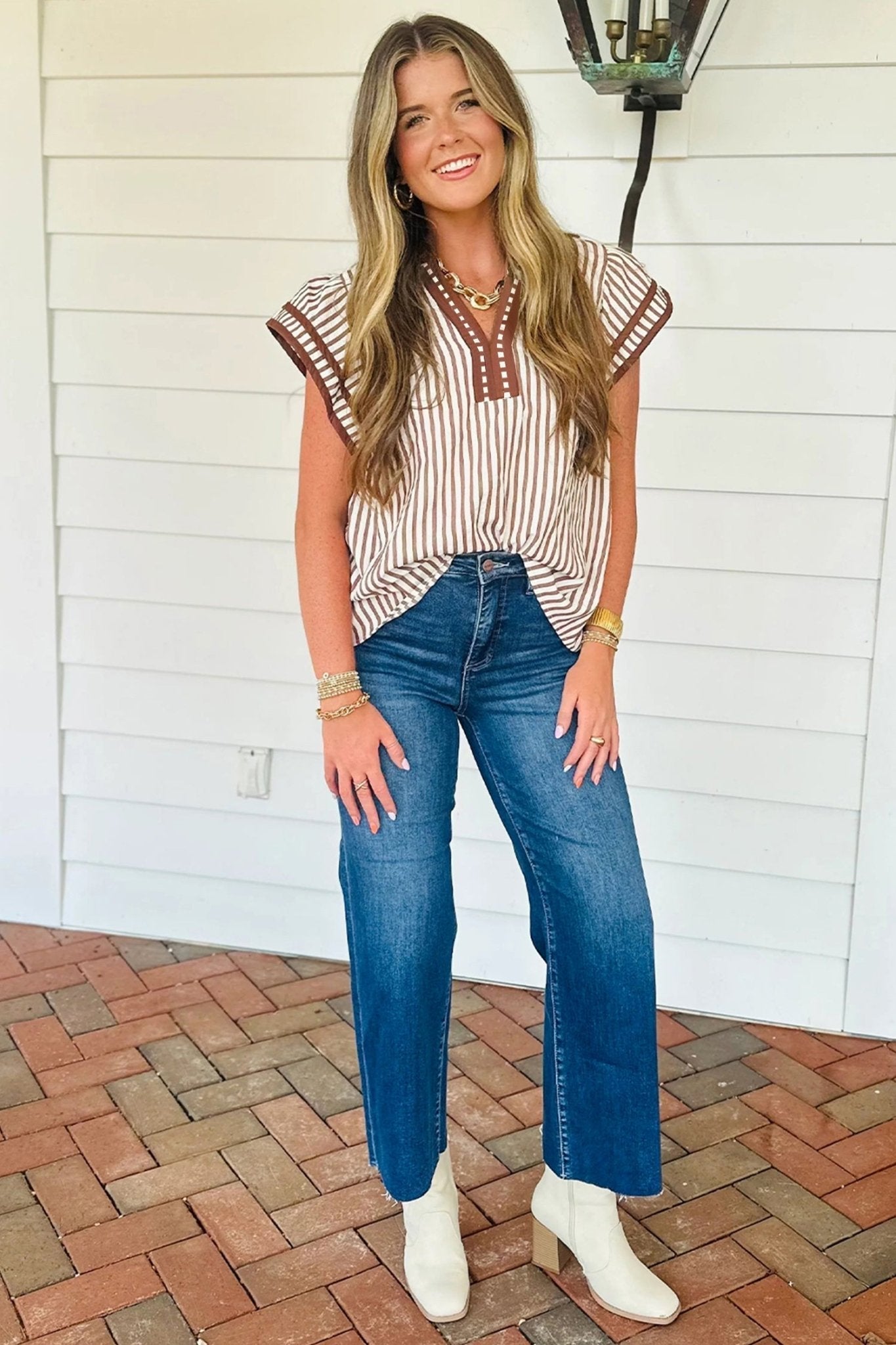 Woman wearing a striped top and blue jeans standing on a brick patio.