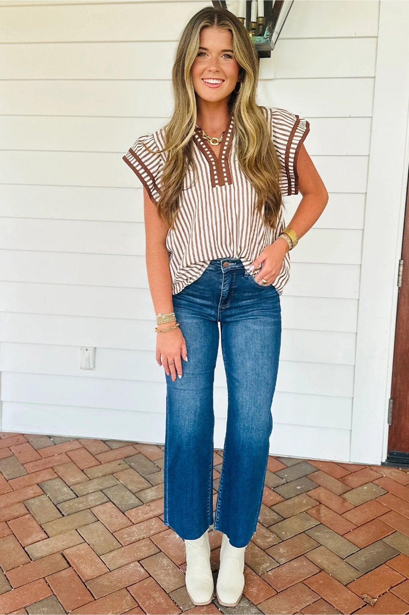 Woman wearing a striped top and blue jeans standing on a brick patio.