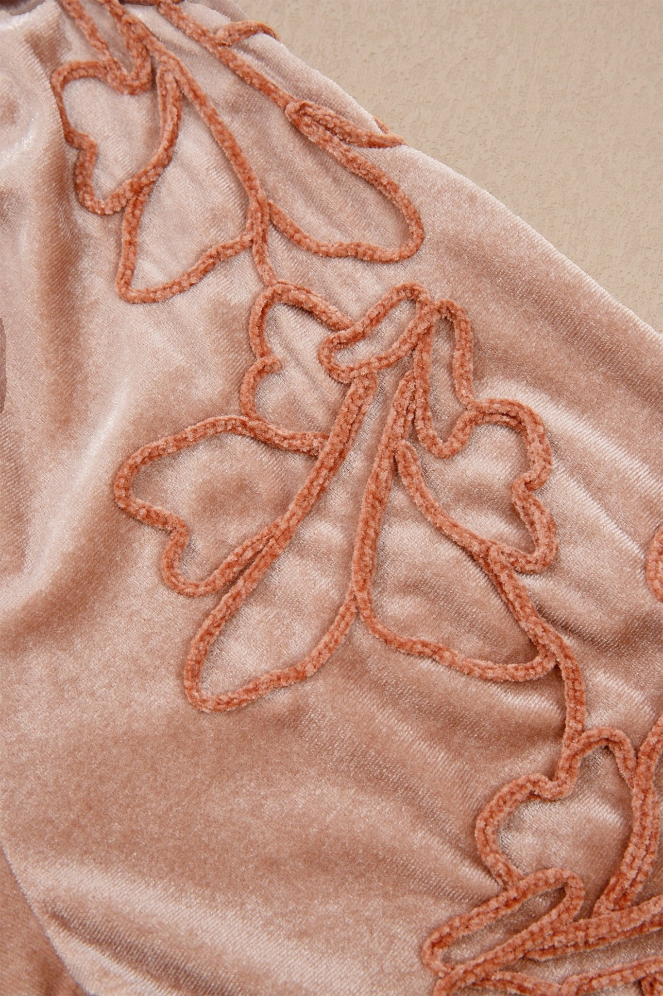 Close-up of dusty rose velvet with terracotta floral embroidery.
