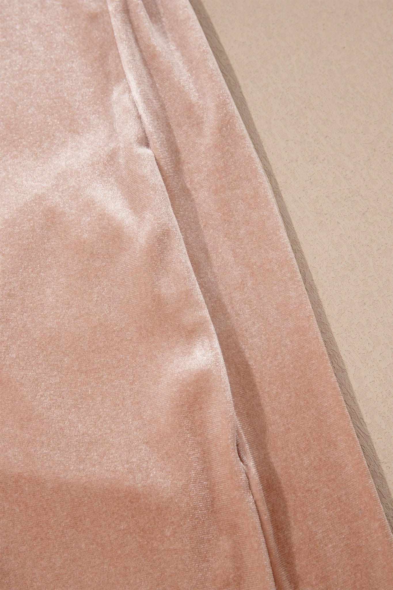 A close-up of a dusty pink velvet fabric, showing its soft texture and sheen, laid next to a neutral beige surface.