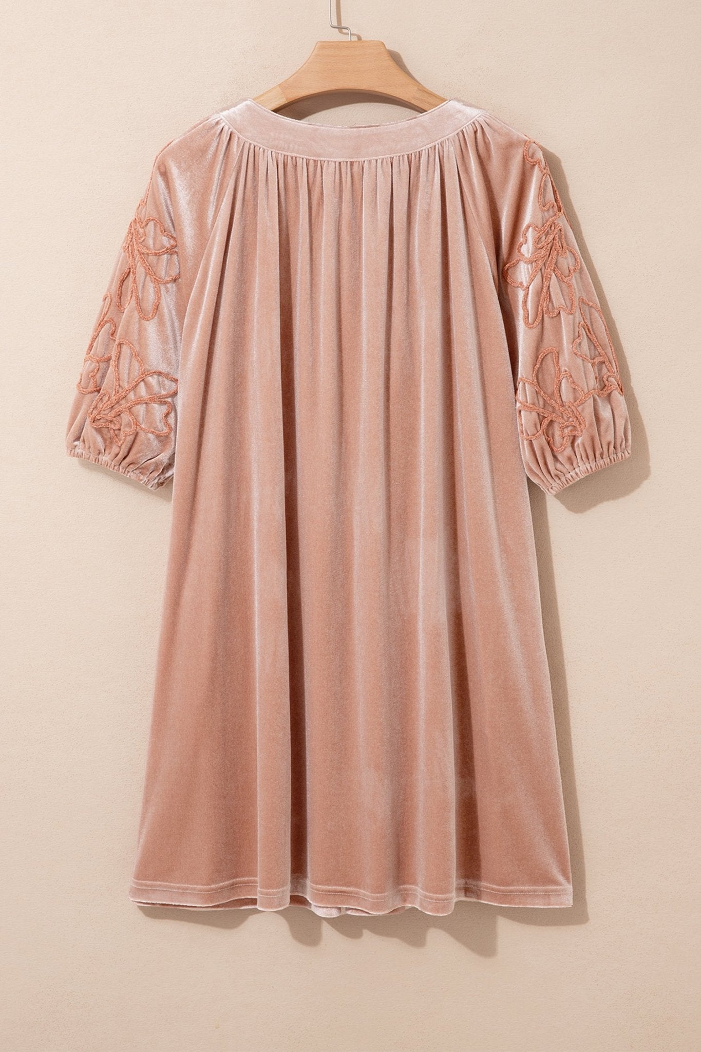 Dusty pink velvet dress with floral-embroidered 3/4 sleeves on hanger against beige wall.