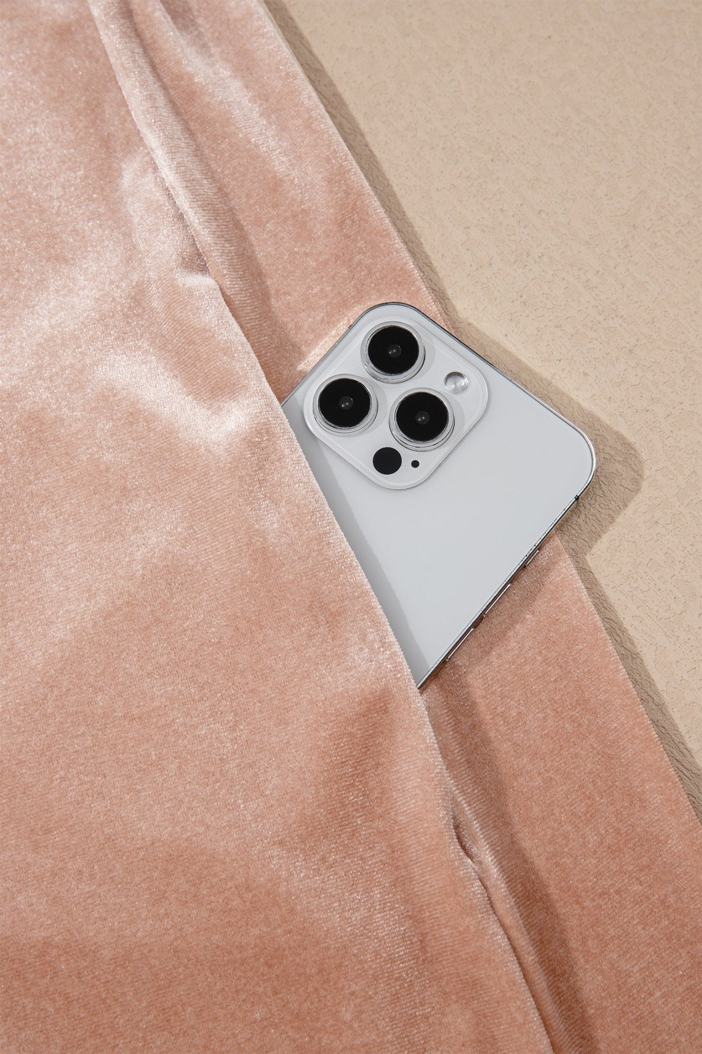 Silver smartphone peeking from peach-pink velvet pocket on beige background.