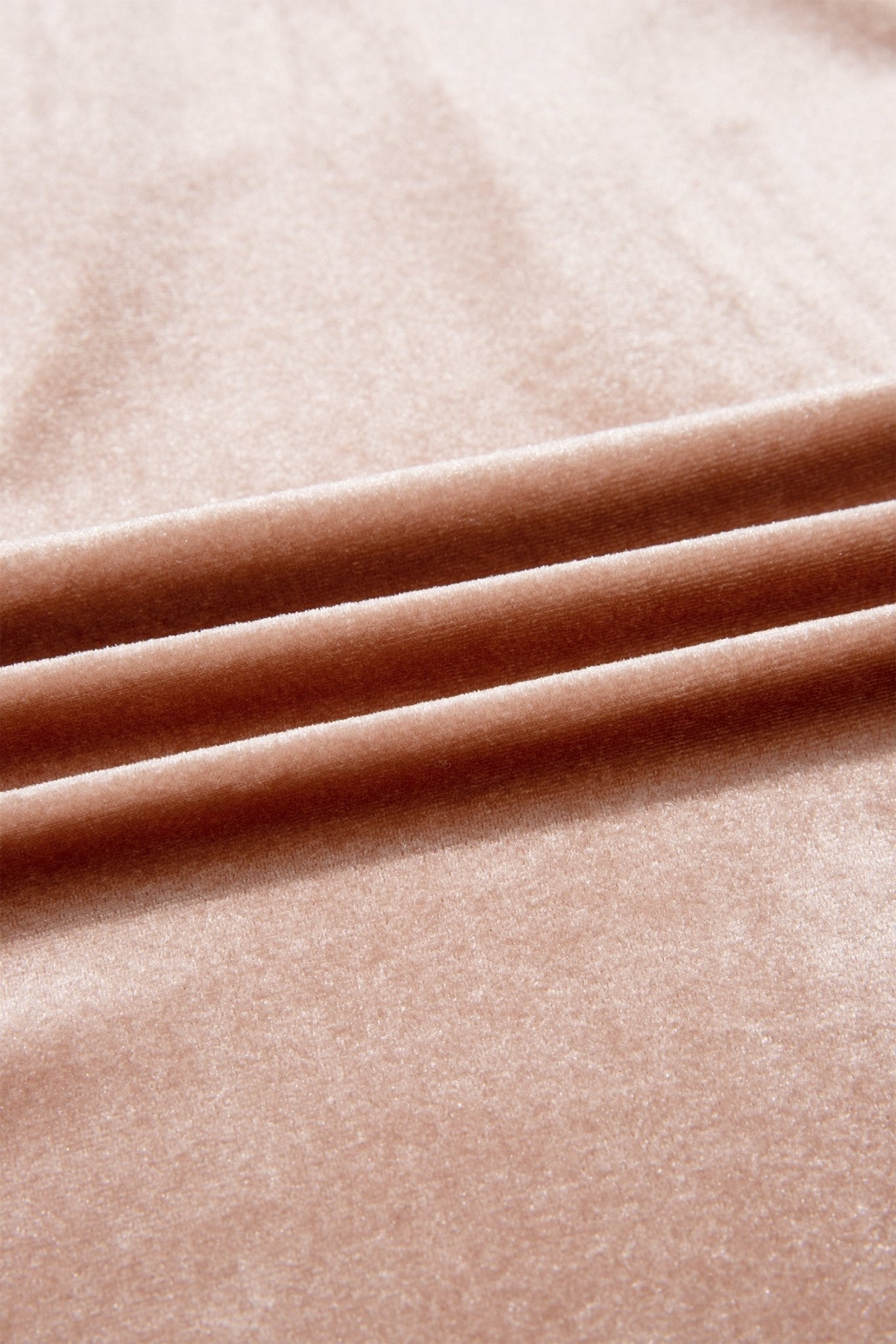 A close-up of soft blush pink velvet fabric with three horizontal folds showing its smooth, plush texture.