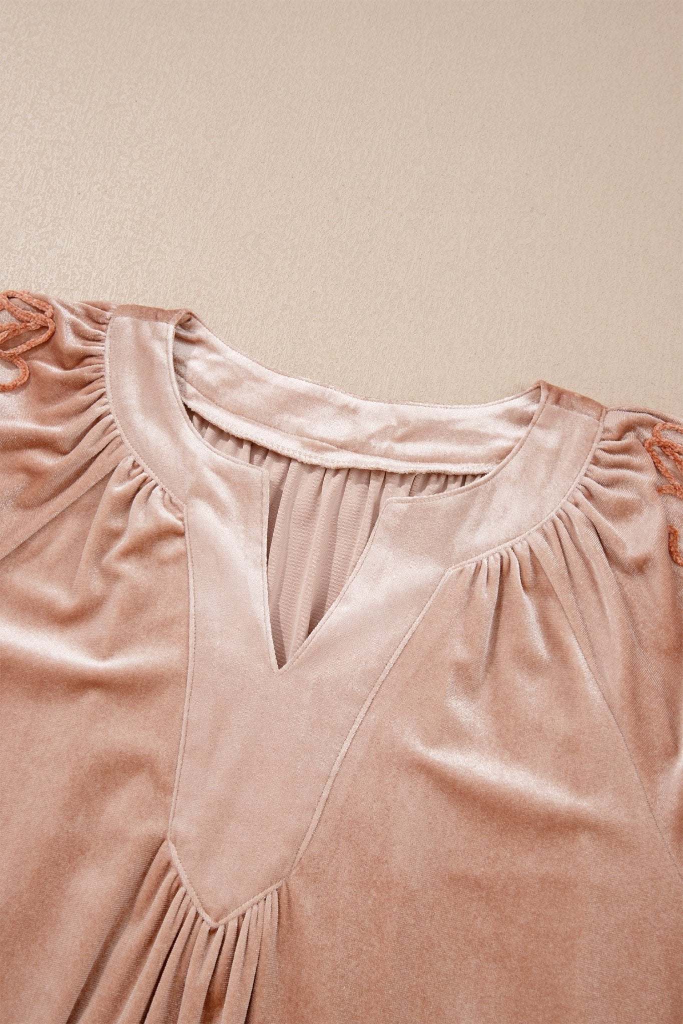 Close-up of dusty rose velvet top with gathered ruffles and split V-neckline against beige background.