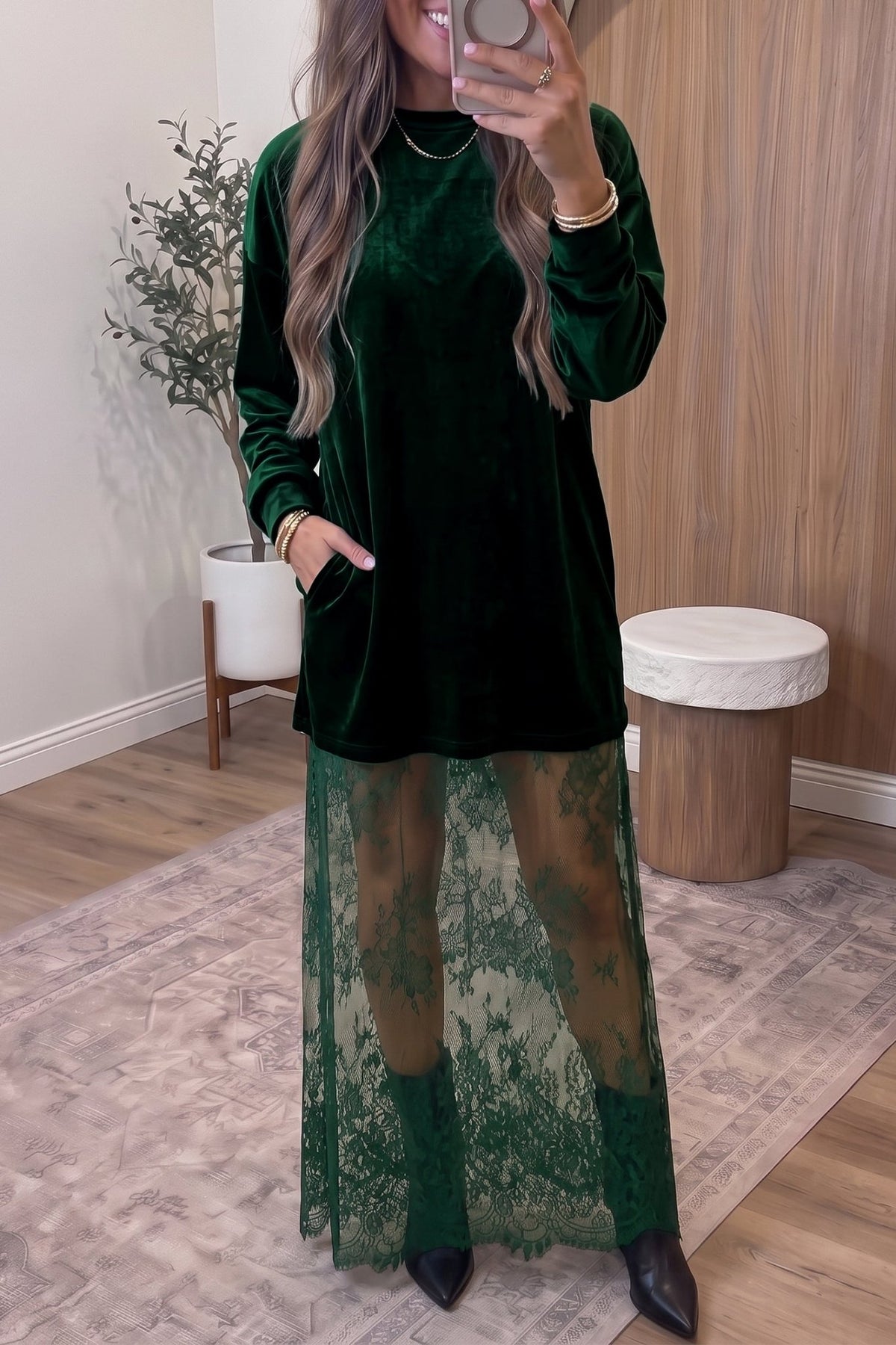 Woman in dark green velvet dress with sheer lace overlay and black boots.