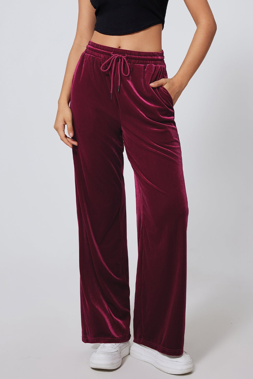 Person in deep burgundy velvet wide-leg pants with black crop top and sneakers.
