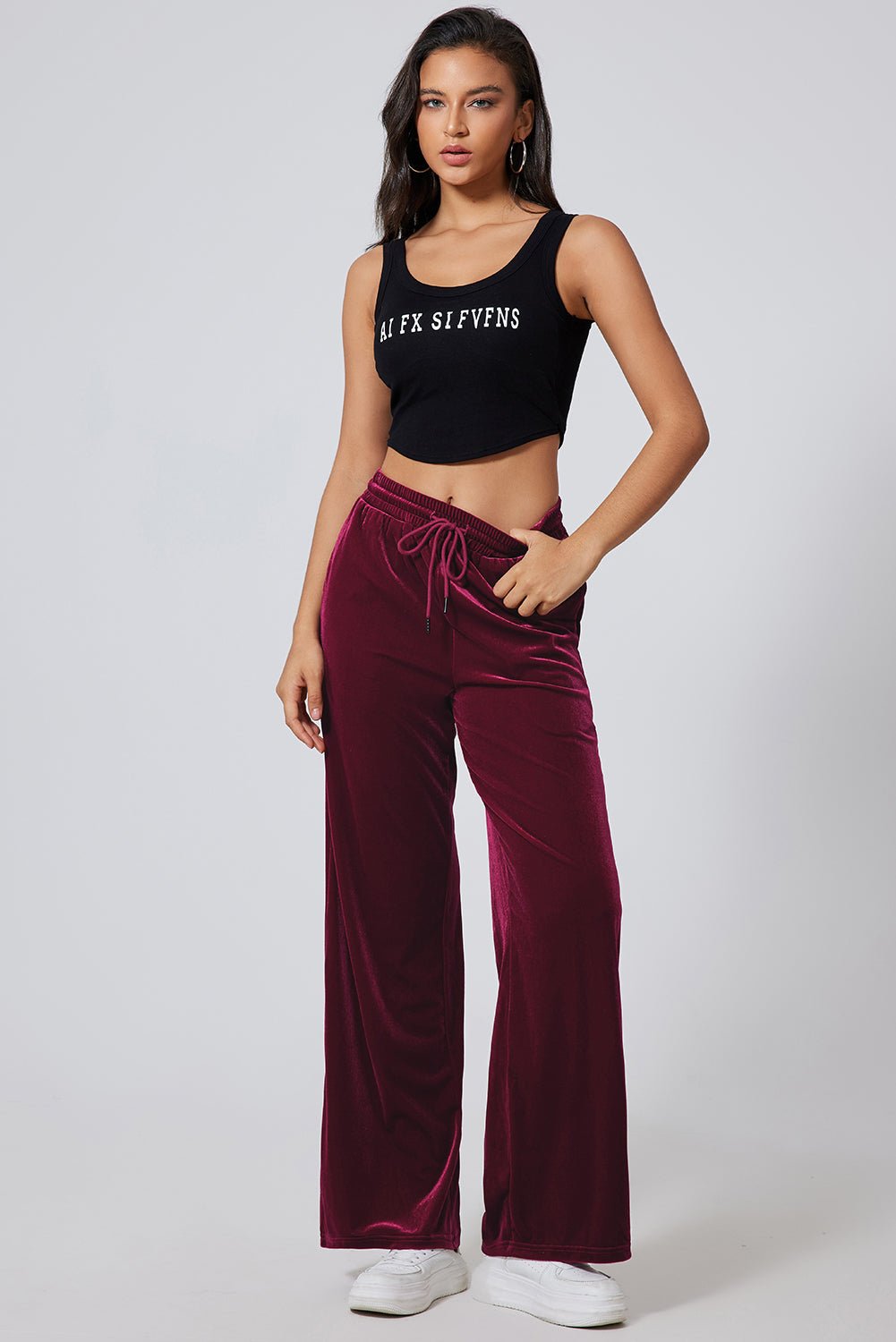 Woman wearing a black tank top and burgundy velvet pants on a white background