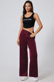 Woman wearing a black tank top and burgundy velvet pants on a white background