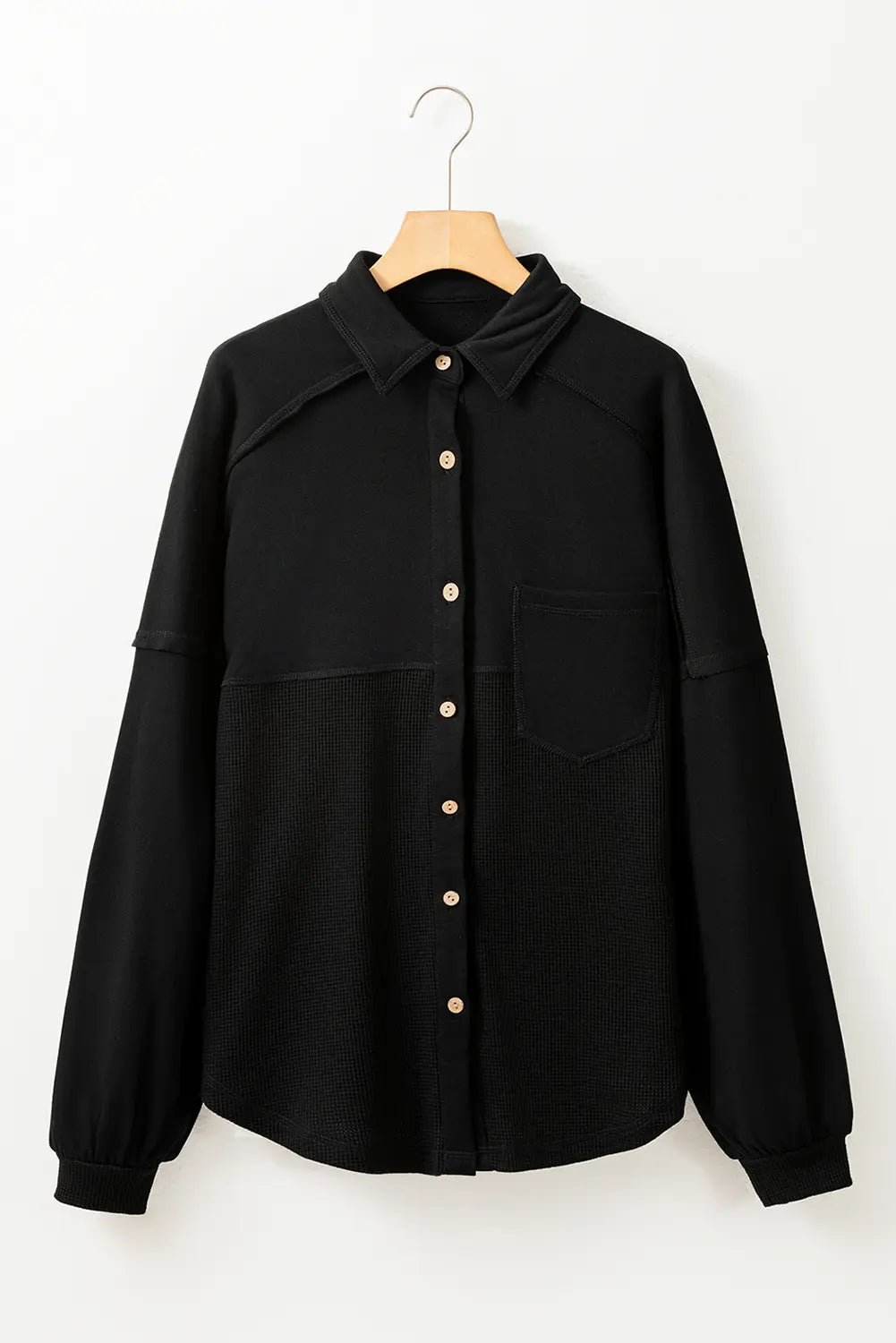 Black shirt with buttons on a wooden hanger against a white background
