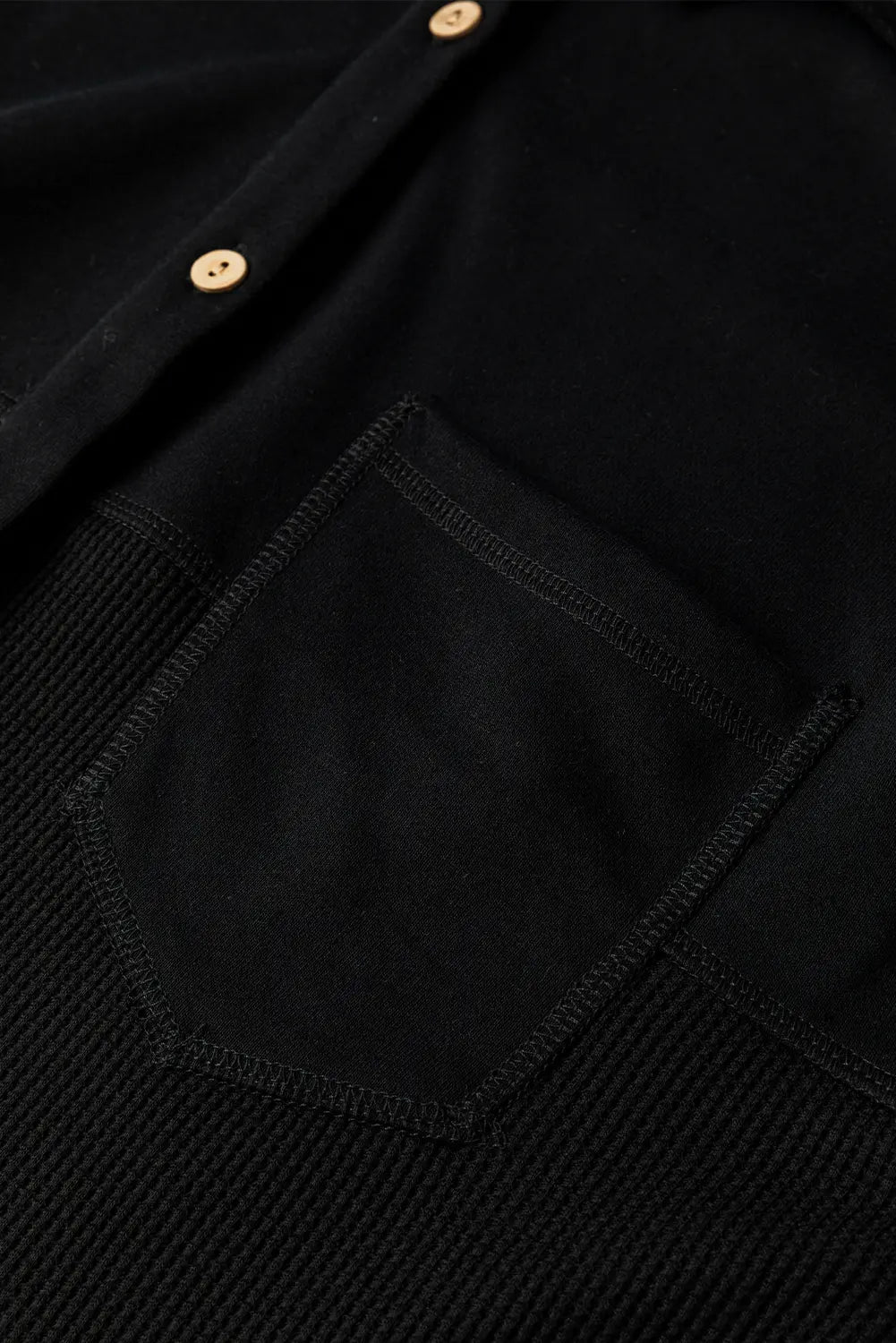 Close-up detail of a black textured knit button-up shirt with a solid black fabric chest pocket and small gold-tone buttons.