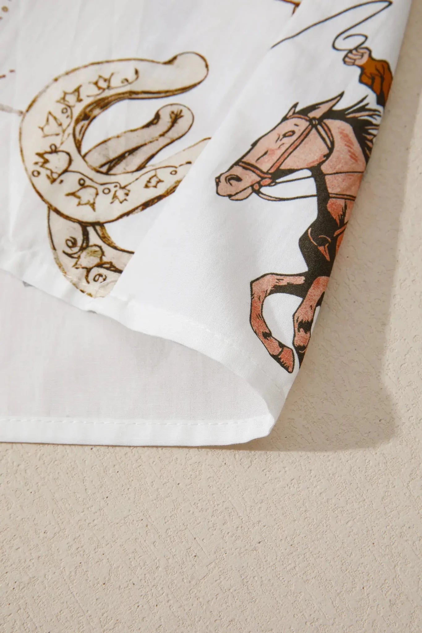 Close-up of a white fabric product, likely a shirt or towel, featuring a printed design of a brown horse and rider with a horseshoe motif.