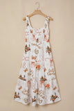 A white sleeveless sundress with a smocked bodice and tiered skirt, featuring an all-over whimsical print of fairies, bows, and autumn motifs in orange, brown, and beige, hanging on a wooden hanger against a solid beige wall.