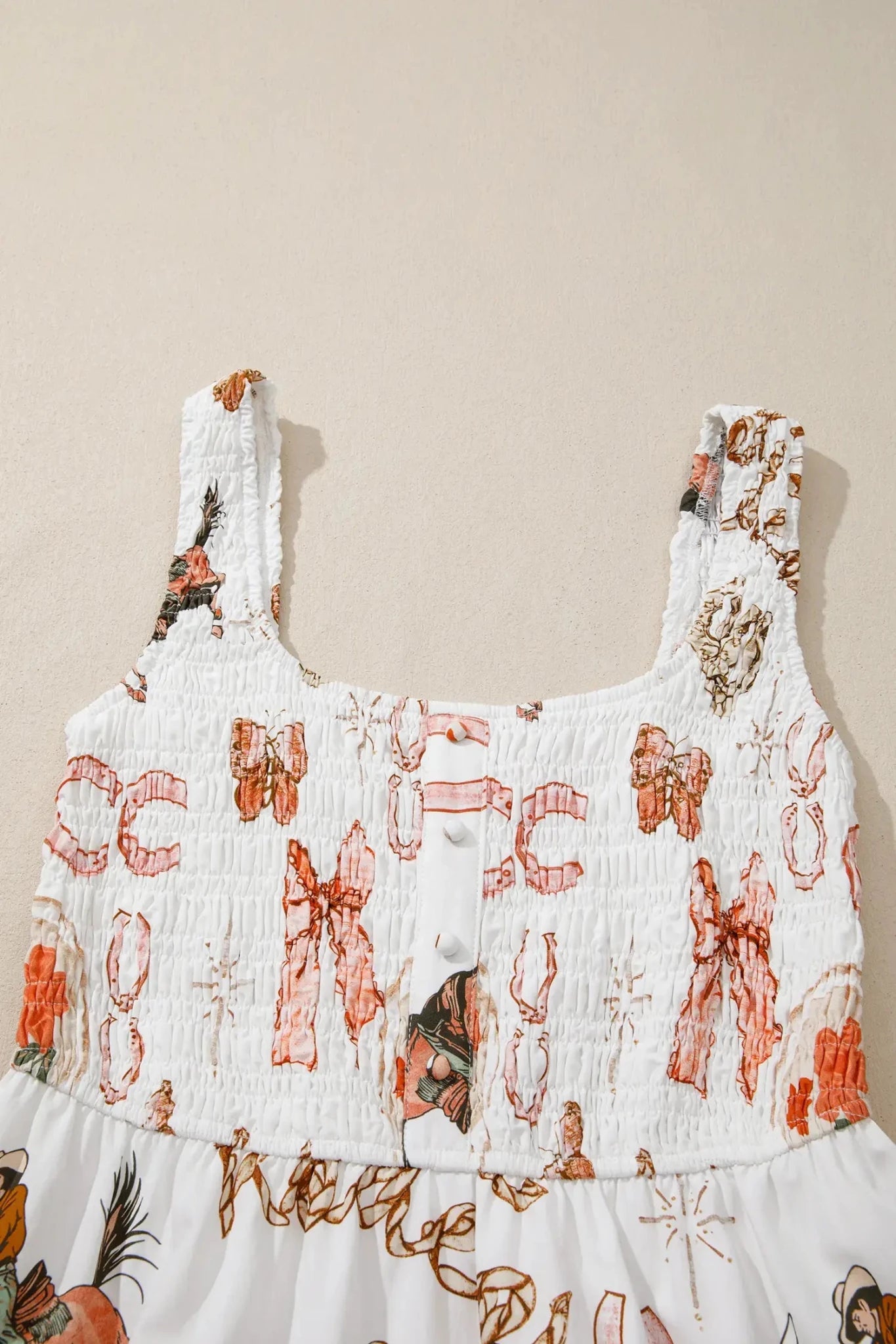 White smocked sleeveless top with an orange and brown bow and floral pattern, shown against a plain beige background.