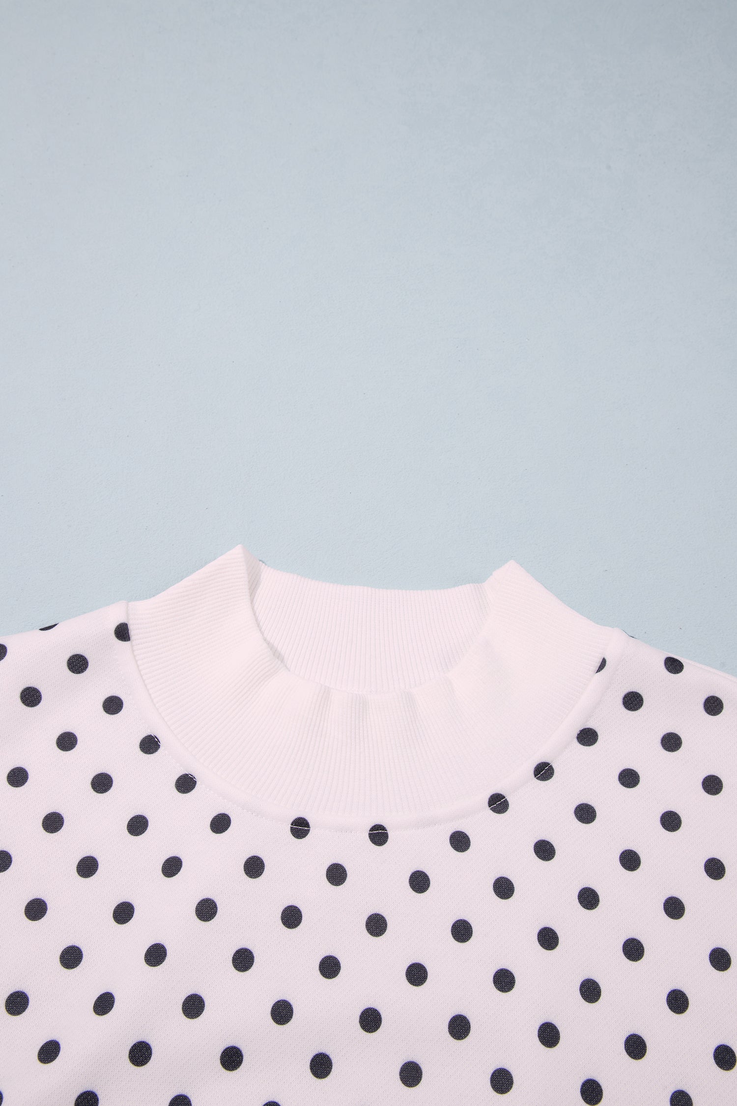 Mock neck detail on white polka dot sweatshirt, close-up