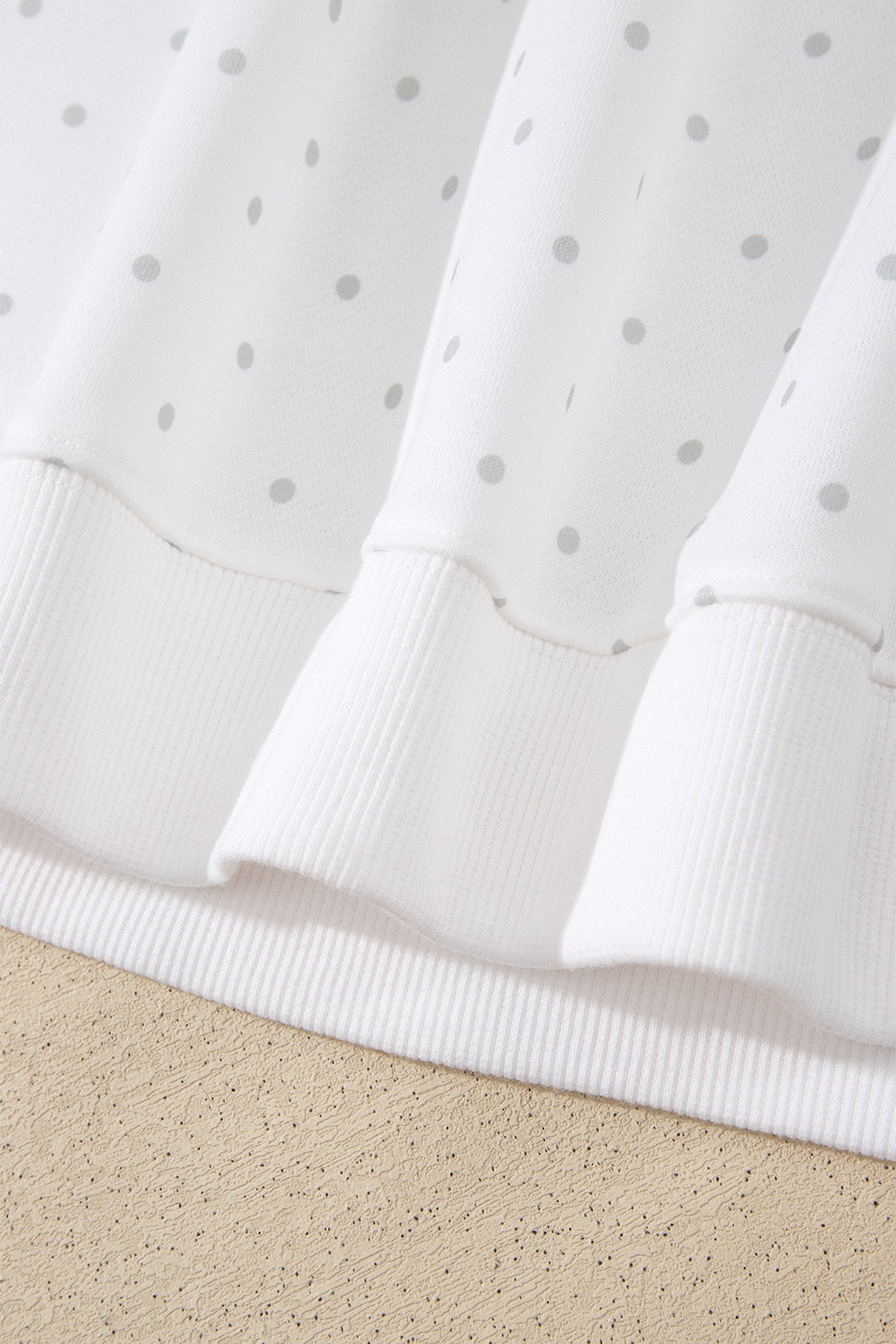 Ribbed hem band on white polka dot sweatshirt, close-up