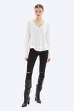 Woman wearing a white long-sleeve top, black ripped jeans, and black knee-high boots on a white background