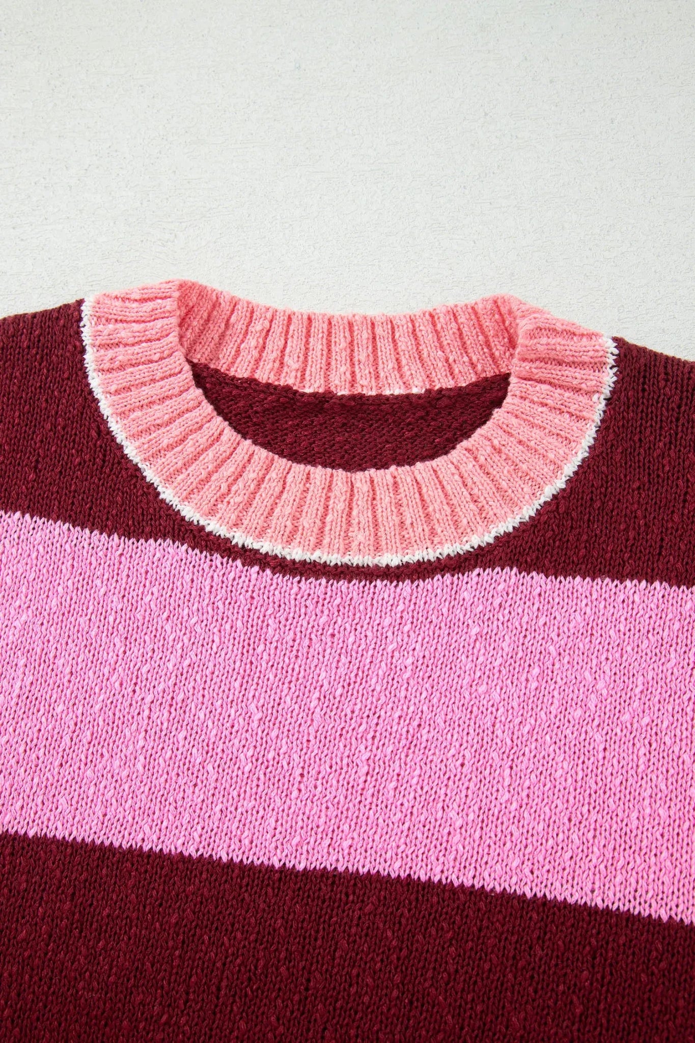 Close-up of striped knit sweater with light pink ribbed crew neck, white edge, dark burgundy, and medium pink stripes.