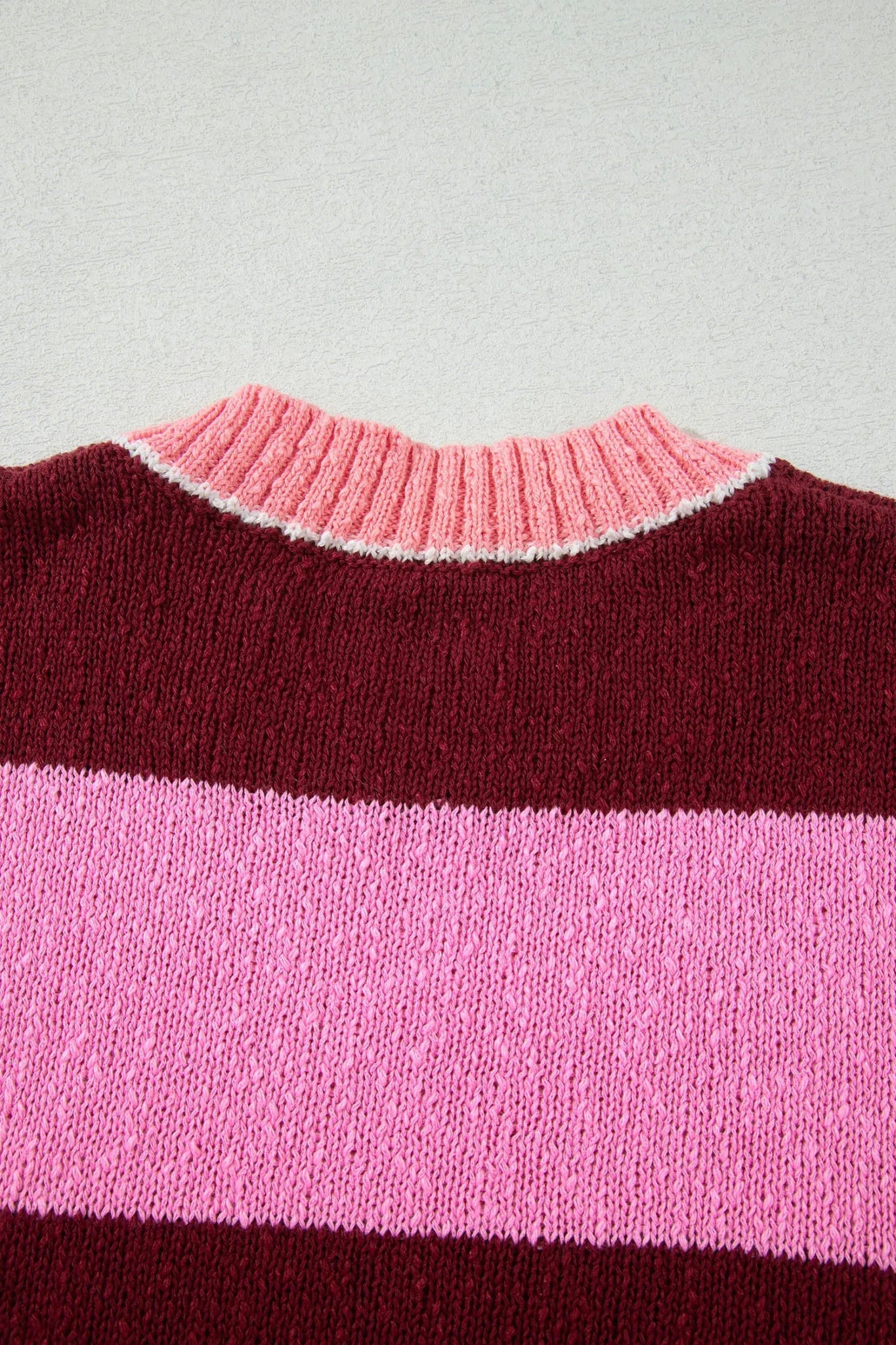 Close-up of striped knit sweater with burgundy top, wide light pink stripe, thin white accent, and pink ribbed crew neck.