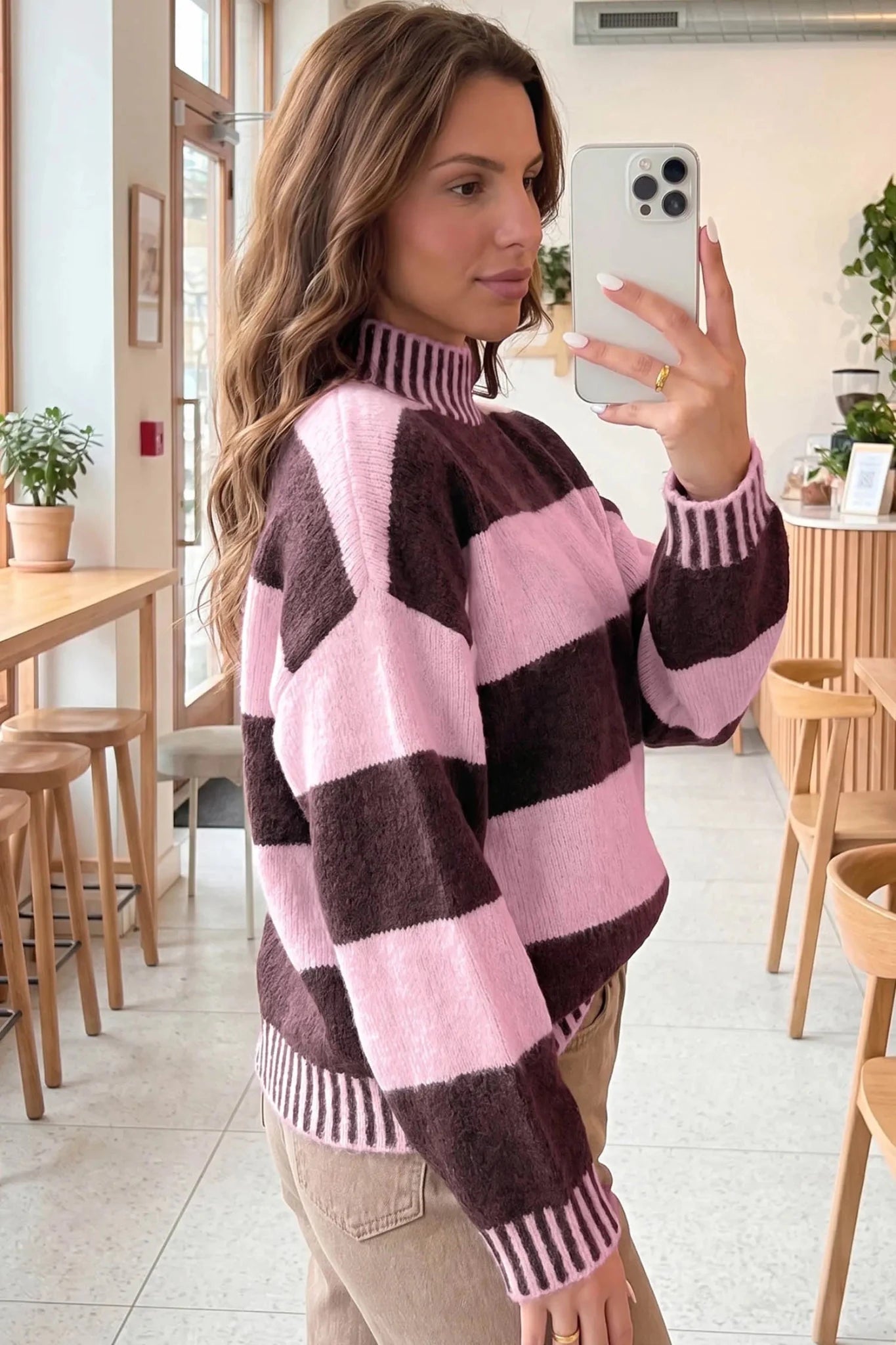 A woman takes a mirror selfie in a cafe while wearing a fuzzy knit mock-neck sweater with large pink and dark brown blocks.