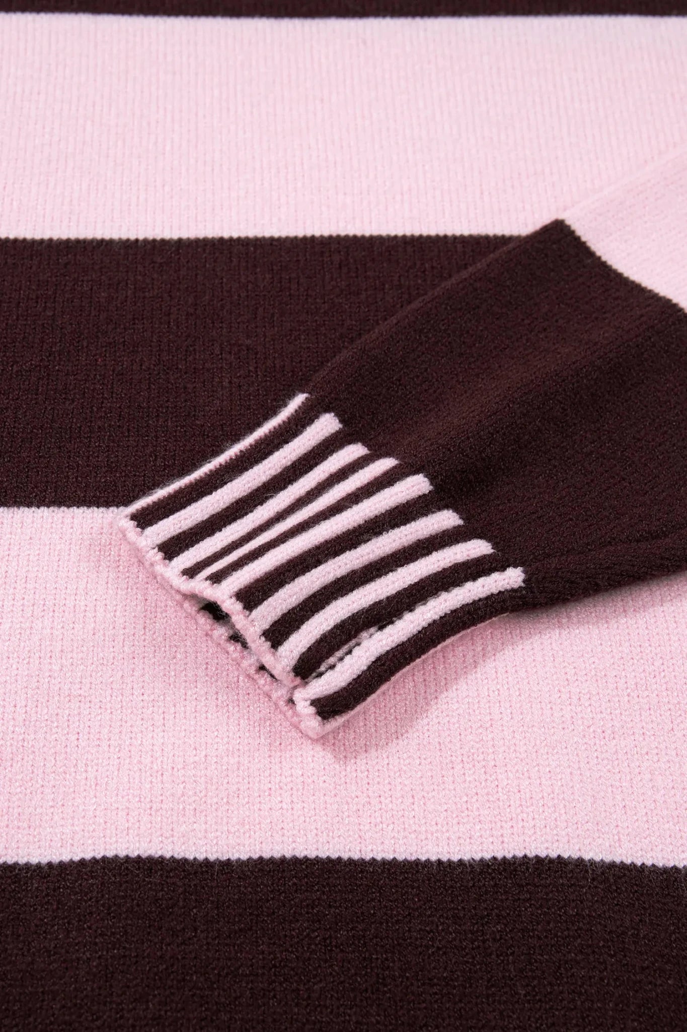 Close-up of a knit garment with wide pink and dark brown stripes and a ribbed striped cuff.