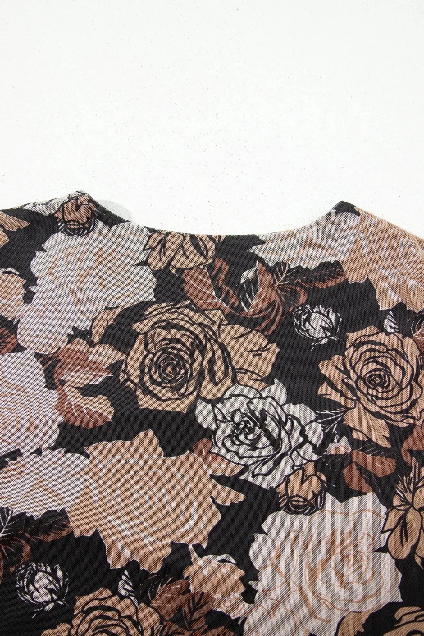 A close-up of a floral-patterned top or dress featuring large roses in beige, cream, and brown tones on a black background, photographed against a plain white backdrop.