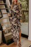 A woman wearing a long-sleeve black maxi dress with a beige and brown floral pattern, holding a glass of wine in an indoor setting with a staircase and glass door.