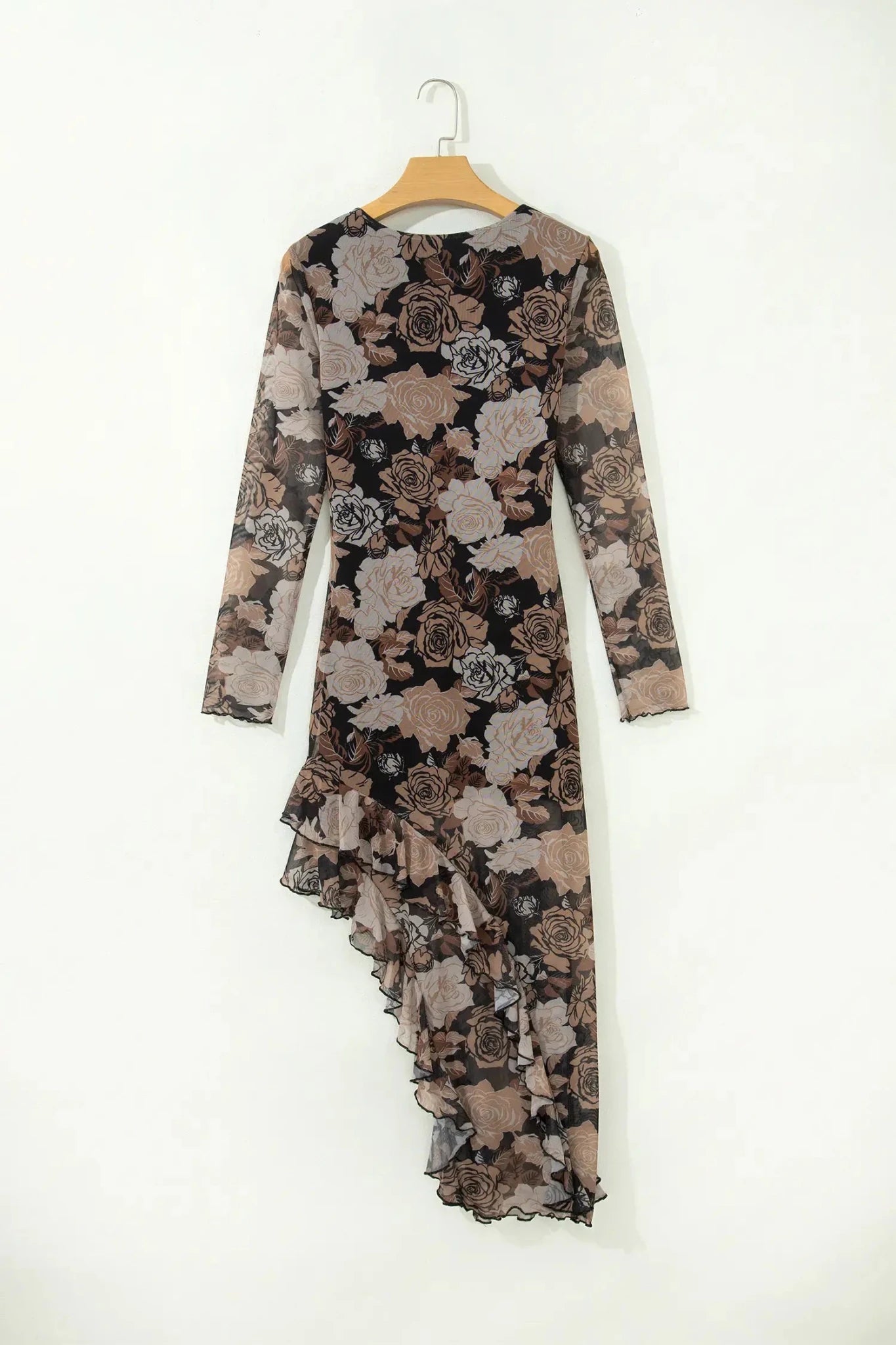 A long-sleeve midi dress with an asymmetrical ruffled hem, featuring a black, brown, and beige floral pattern, hanging on a wooden hanger against a plain white wall.